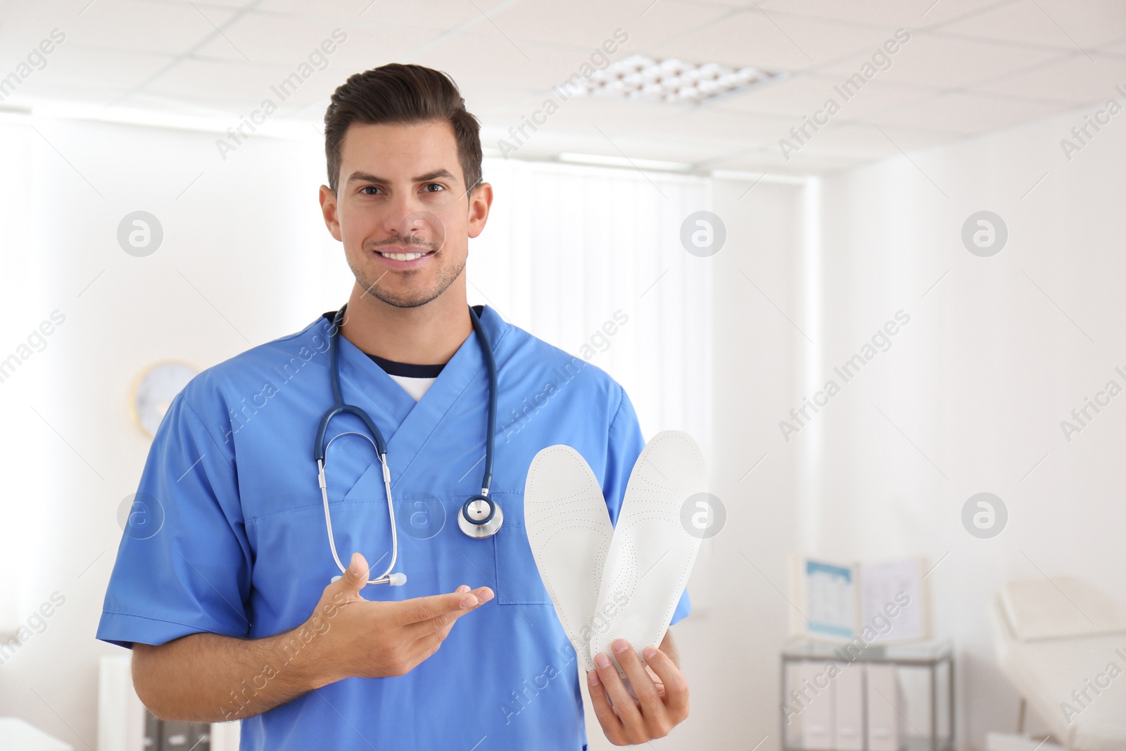 Photo of Handsome male orthopedist showing insoles in clinic