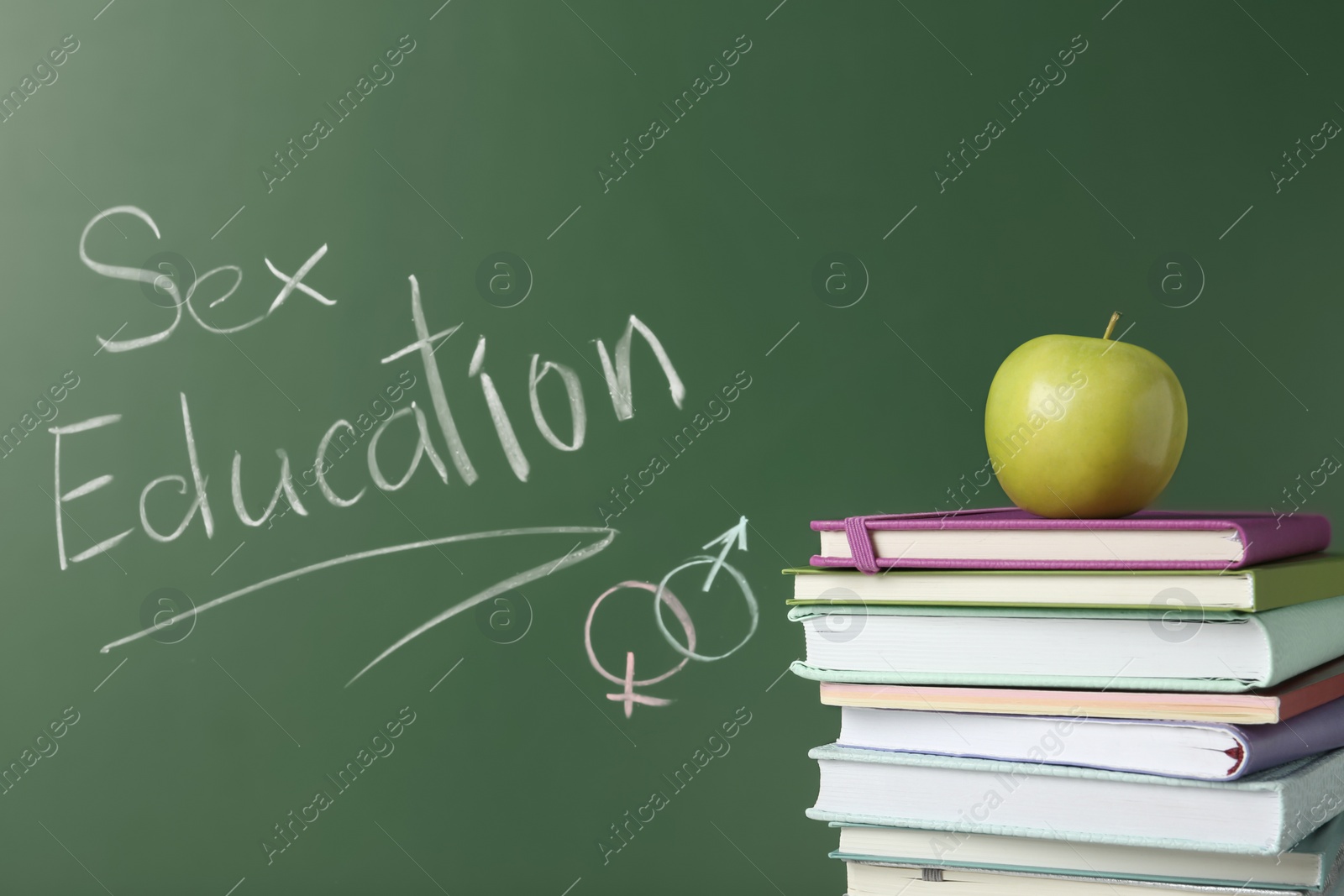 Photo of Books and apple near chalkboard with phrase "Sex education"