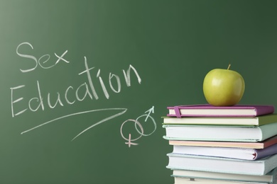 Books and apple near chalkboard with phrase "Sex education"