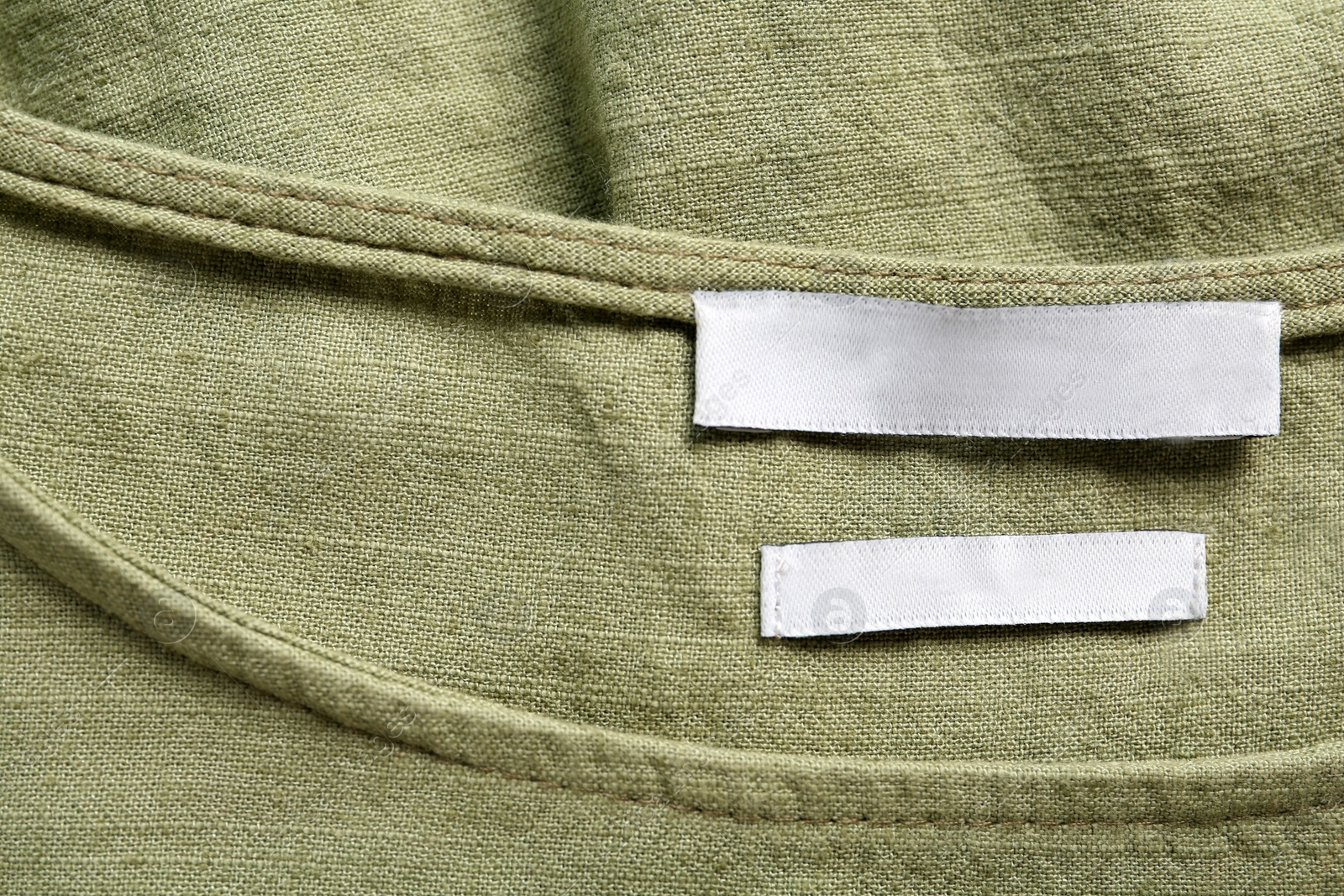 Photo of Blank clothing label on green apparel, top view. Space for text