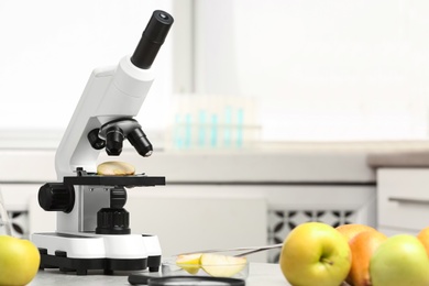 Microscope with slice of apple on table in laboratory, space for text. Poison detection