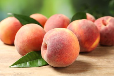 Many whole fresh ripe peaches and green leaves on wooden table against blurred background, closeup