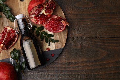 Photo of Tasty pomegranate sauce in bottle, fruits and branches on wooden table, top view. Space for text