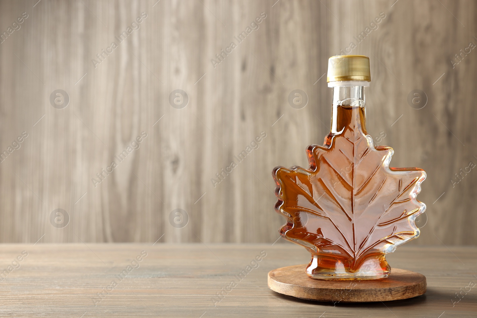 Photo of Leaf shaped bottle of tasty maple syrup on wooden table, space for text