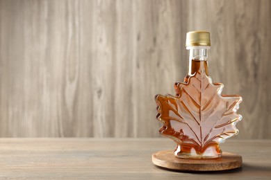 Leaf shaped bottle of tasty maple syrup on wooden table, space for text