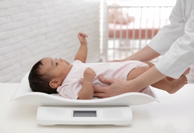 Doctor weighting African-American baby on scales in light room