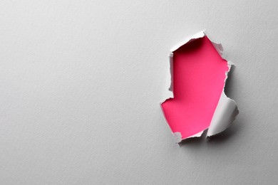 Photo of Hole in white paper on pink background, space for text