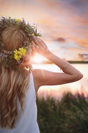 Photo of Young woman wearing wreath madebeautiful flowers outdoors at sunset