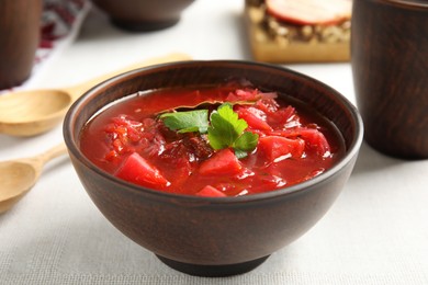 Photo of Stylish brown clay bowl with Ukrainian borsch served on white tablecloth, closeup