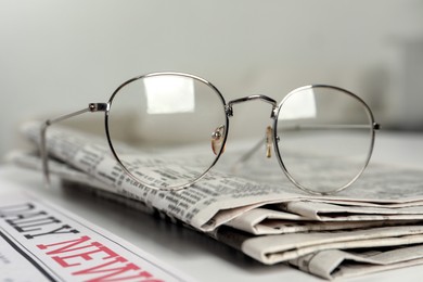 Glasses on stack of newspapers indoors, closeup