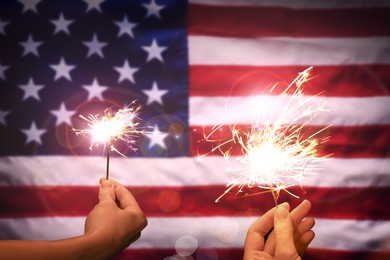 Image of 4th of July - Independence Day of USA. Women holding burning sparklers against American flag, closeup