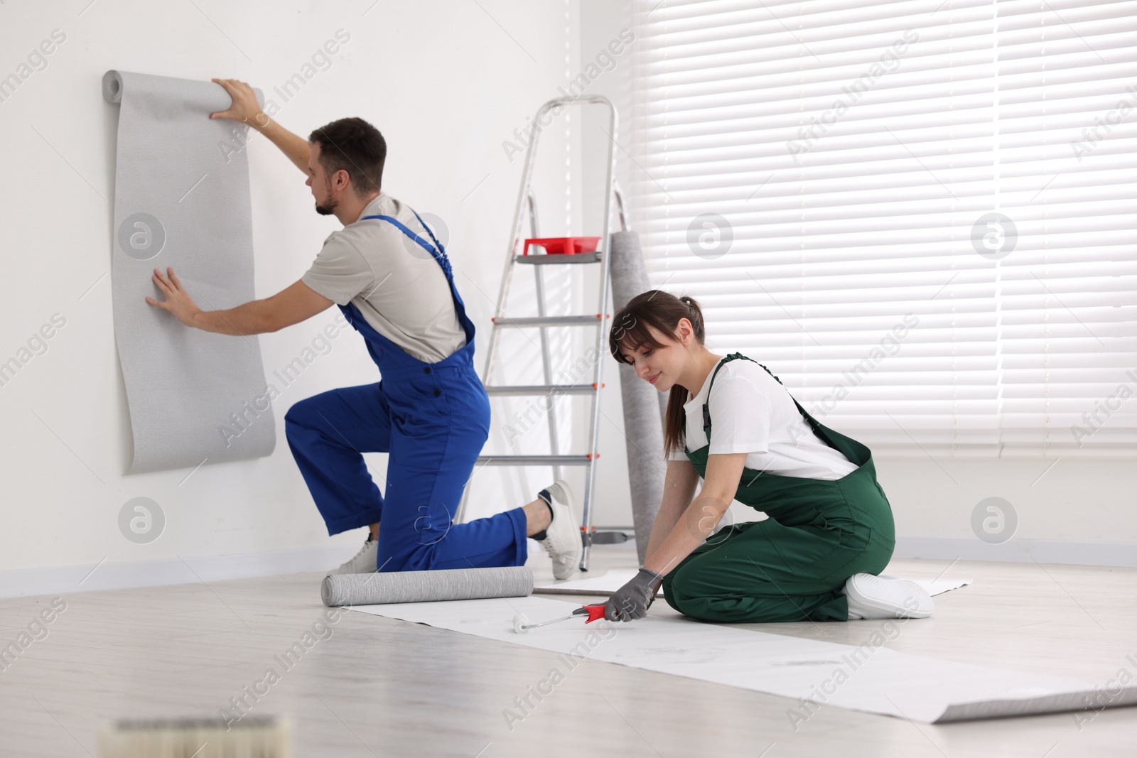 Photo of Woman applying glue onto wallpaper while man hanging sheet indoors