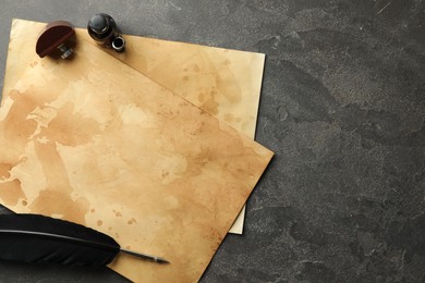 Photo of Black feather, inkwell and vintage parchment on grey table, flat lay