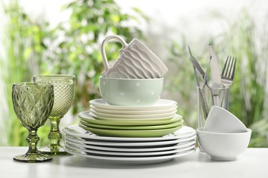 Beautiful ceramic dishware, glasses, cutlery and cup on white marble table outdoors