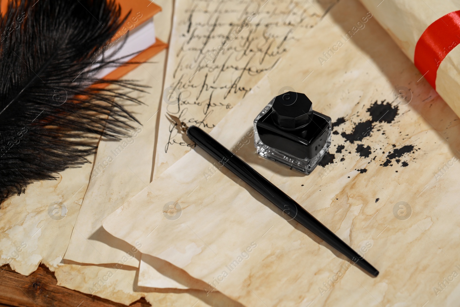 Photo of Inkwell, feather, fountain pen and vintage parchment on wooden table, above view