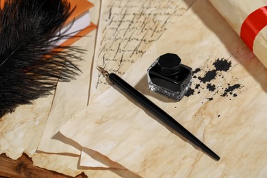 Inkwell, feather, fountain pen and vintage parchment on wooden table, above view