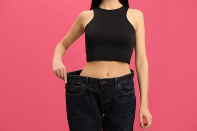 Photo of Young woman wearing big jeans after weight loss on pink background, closeup