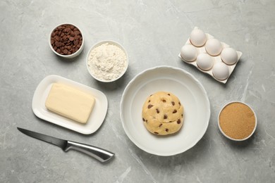 Fresh dough and different ingredients for cooking chocolate chip cookies on light grey marble table, flat lay