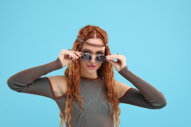 Photo of Stylish young hippie woman in sunglasses on light blue background