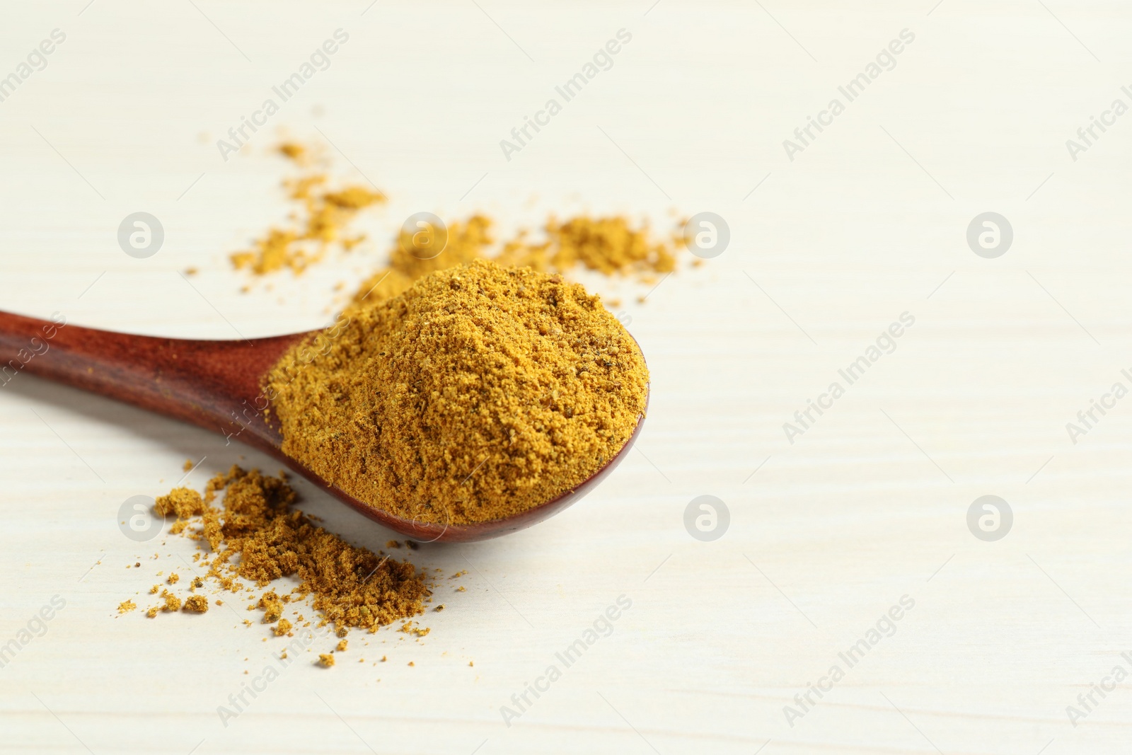 Photo of Spoon with dry curry powder on light wooden table, closeup. Space for text