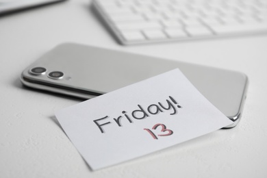 Photo of Paper note with phrase Friday 13 and smartphone on white table. Superstition of bad luck