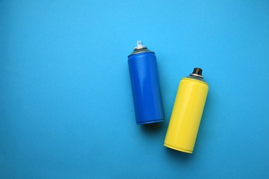 Cans of different graffiti spray paints on light blue background, flat lay. Space for text