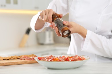 Photo of Professional chef adding pepper to delicious dish at white marble table, closeup