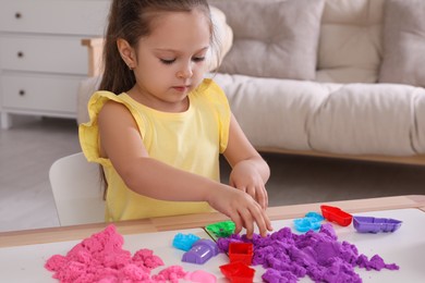 Cute little girl playing with bright kinetic sand at table in room