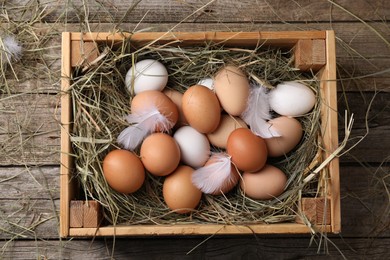 Fresh chicken eggs and dried hay in crate on wooden table, top view