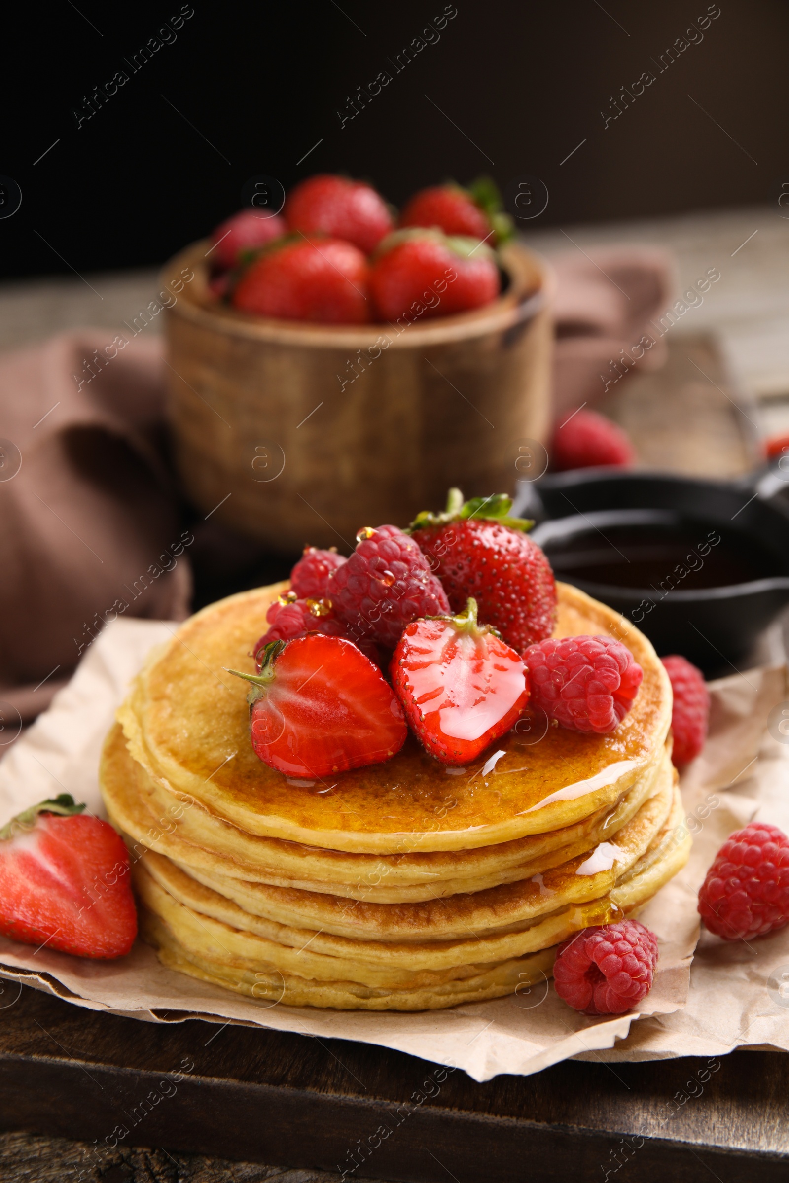 Photo of Tasty pancakes with fresh berries and honey on wooden board, closeup