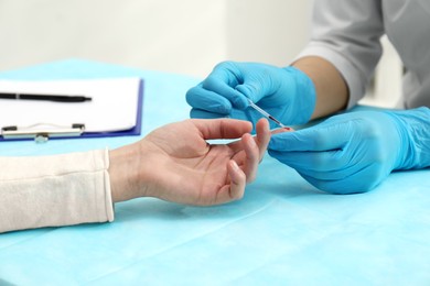 Photo of Doctor taking blood sample from patient's finger at table in clinic, closeup