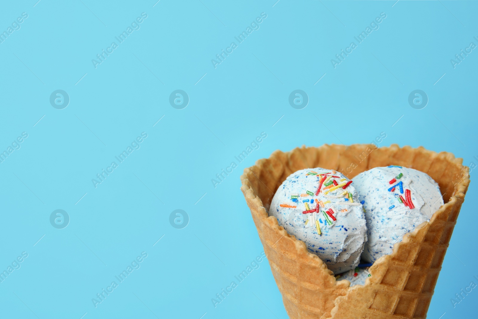 Photo of Delicious ice cream with sprinkles in waffle cone on color background, space for text