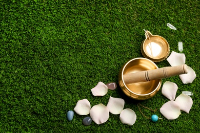 Flat lay composition with golden singing bowl on green grass, flat lay. Sound healing