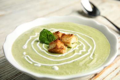 Photo of Delicious broccoli cream soup with croutons served on white wooden table, closeup