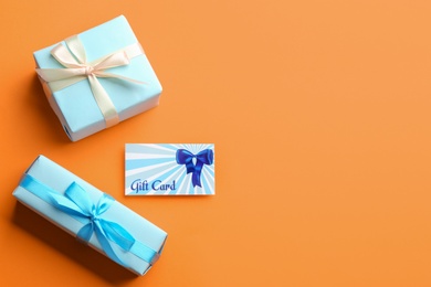 Photo of Gift card and presents on orange background, flat lay. Space for text