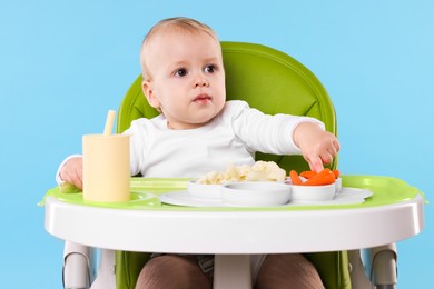 Cute little baby with healthy food in high chair on light blue background