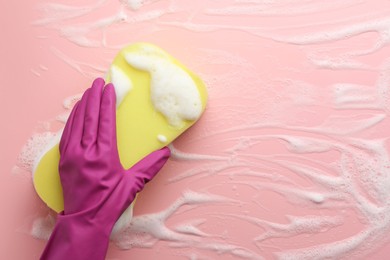 Cleaner in rubber glove holding sponge with foam on pink background, top view.