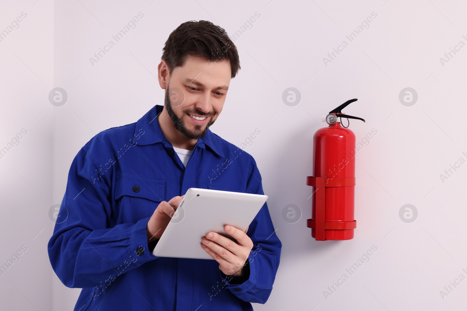 Photo of Man with tablet checking fire extinguisher indoors