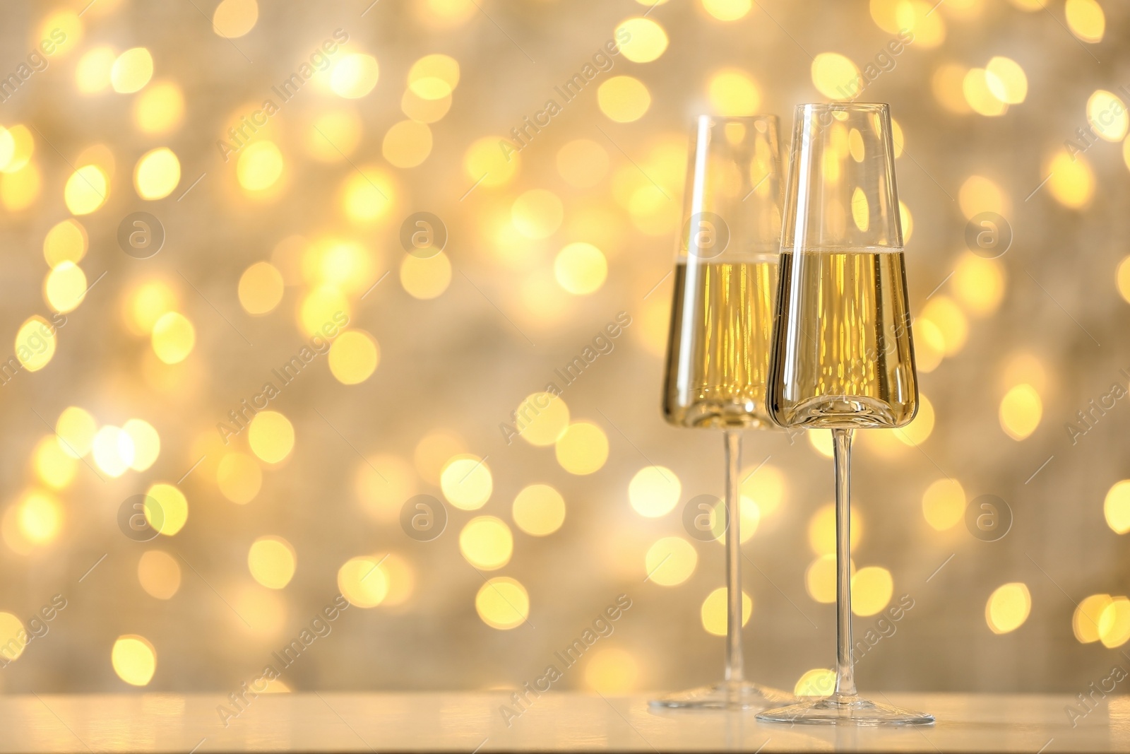 Photo of Glasses of fizzy champagne against blurred fairy lights, space for text