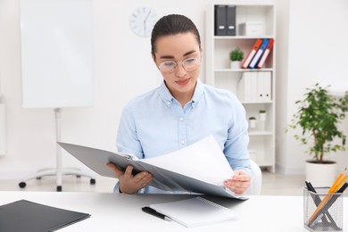 Photo of Young female intern with folder working at table in office