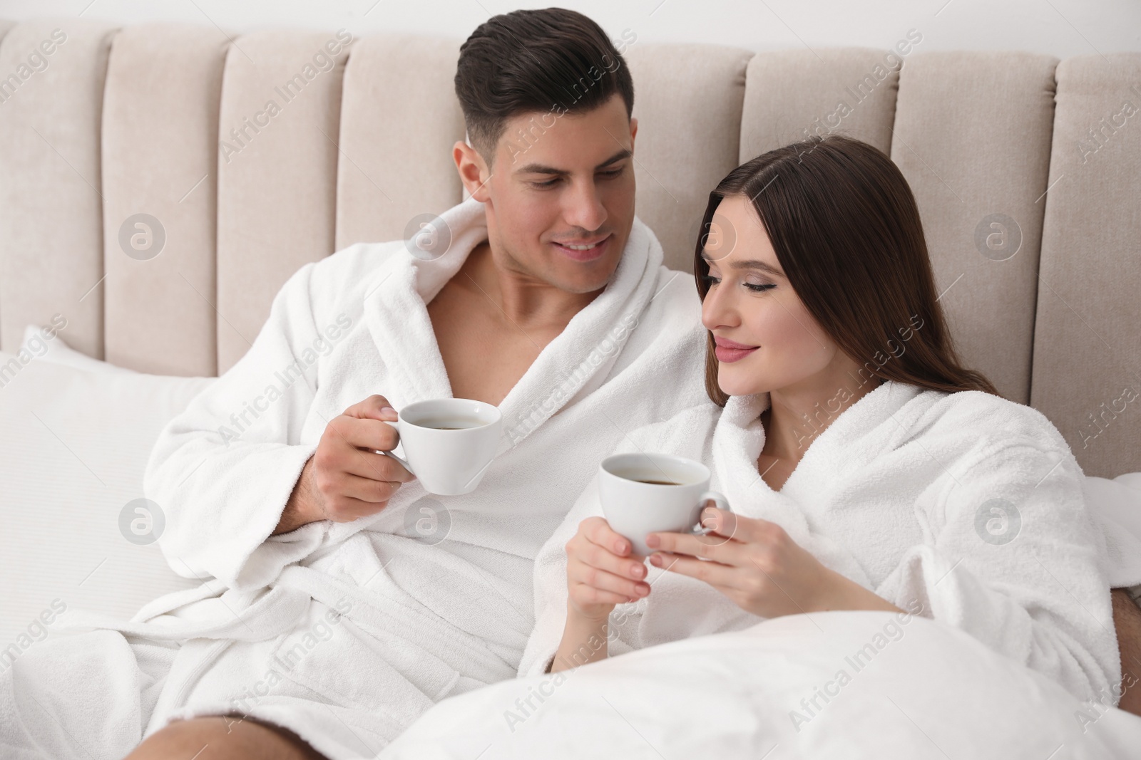 Photo of Happy couple in bathrobes with coffee on bed at home