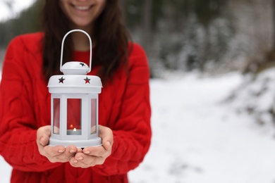 Woman holding lantern with burning candle near snowy forest. Space for text