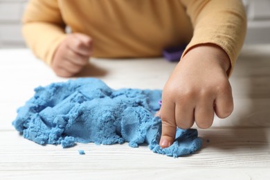 Photo of Little child playing with light blue kinetic sand at white wooden table, closeup