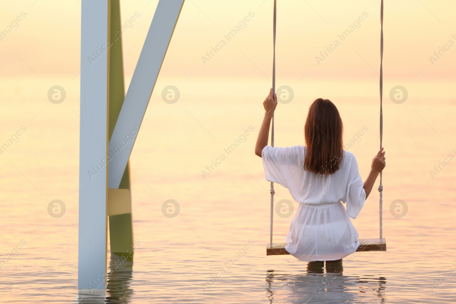 Photo of Young woman enjoying sunrise on swing over water