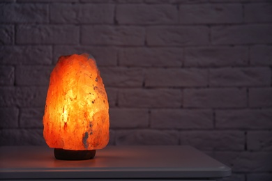 Photo of Himalayan salt lamp glowing on table near brick wall with space for text