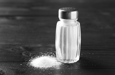 Photo of Organic salt in glass shaker on black wooden table, closeup