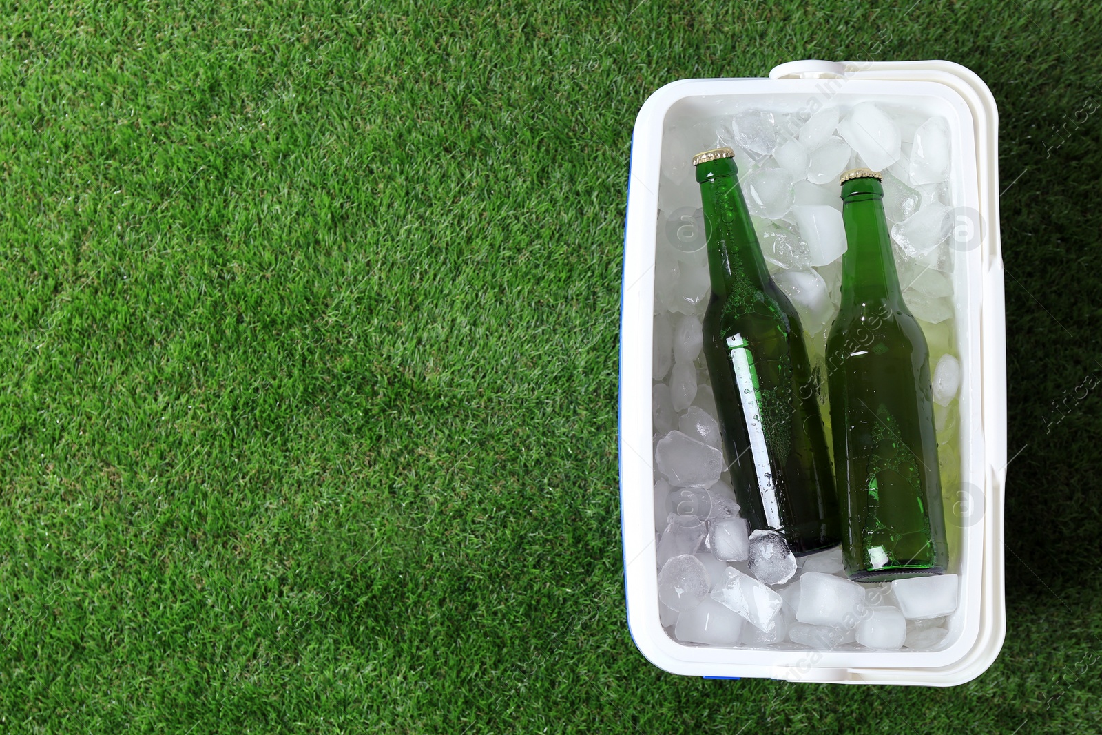 Photo of Plastic cool box with bottles of beer and ice cubes on green grass outdoors, top view. Space for text