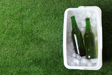 Plastic cool box with bottles of beer and ice cubes on green grass outdoors, top view. Space for text