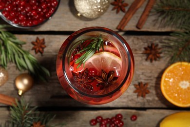 Photo of Glass bottle of aromatic punch drink, ingredients and Christmas decor on wooden table, flat lay