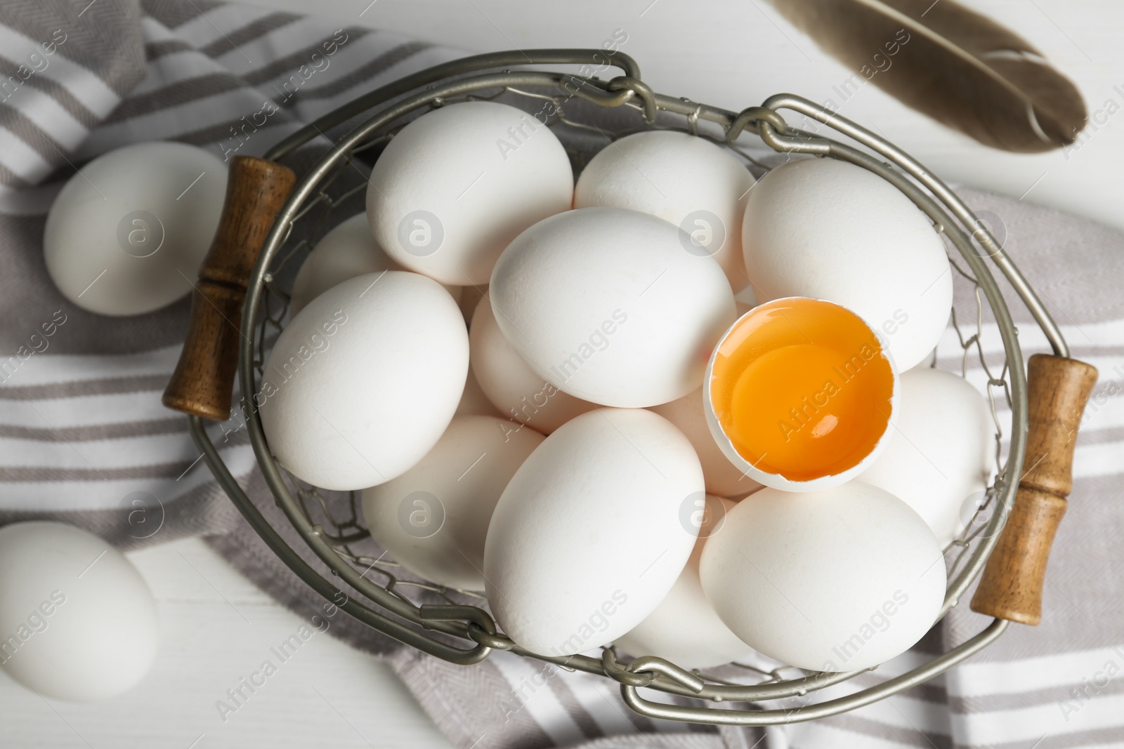 Photo of Many raw chicken eggs in metal basket on white wooden table, flat lay